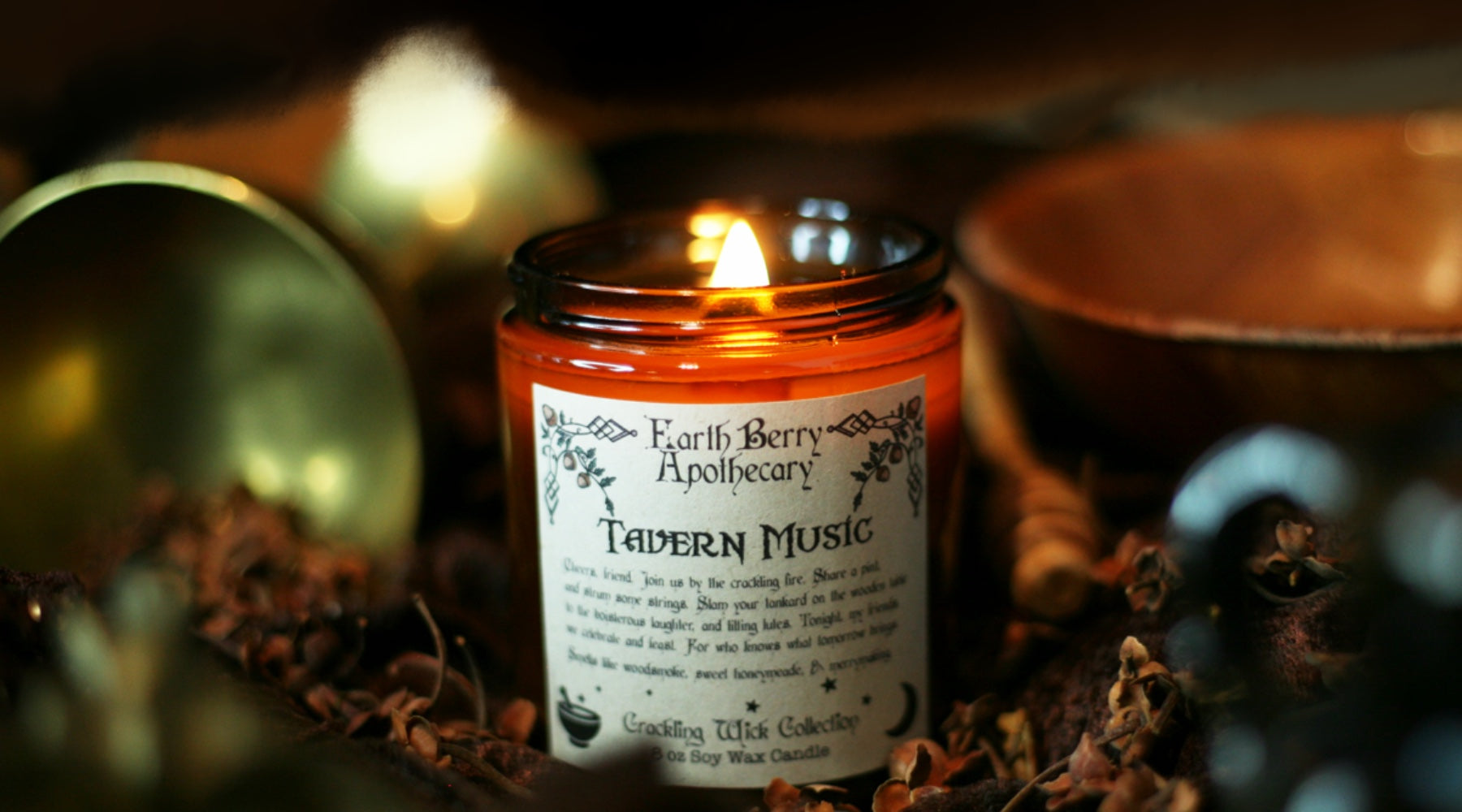 An earthy honey and tobacco scented crackling wick candle in an amber jar with a fantasy theme, called tavern music.