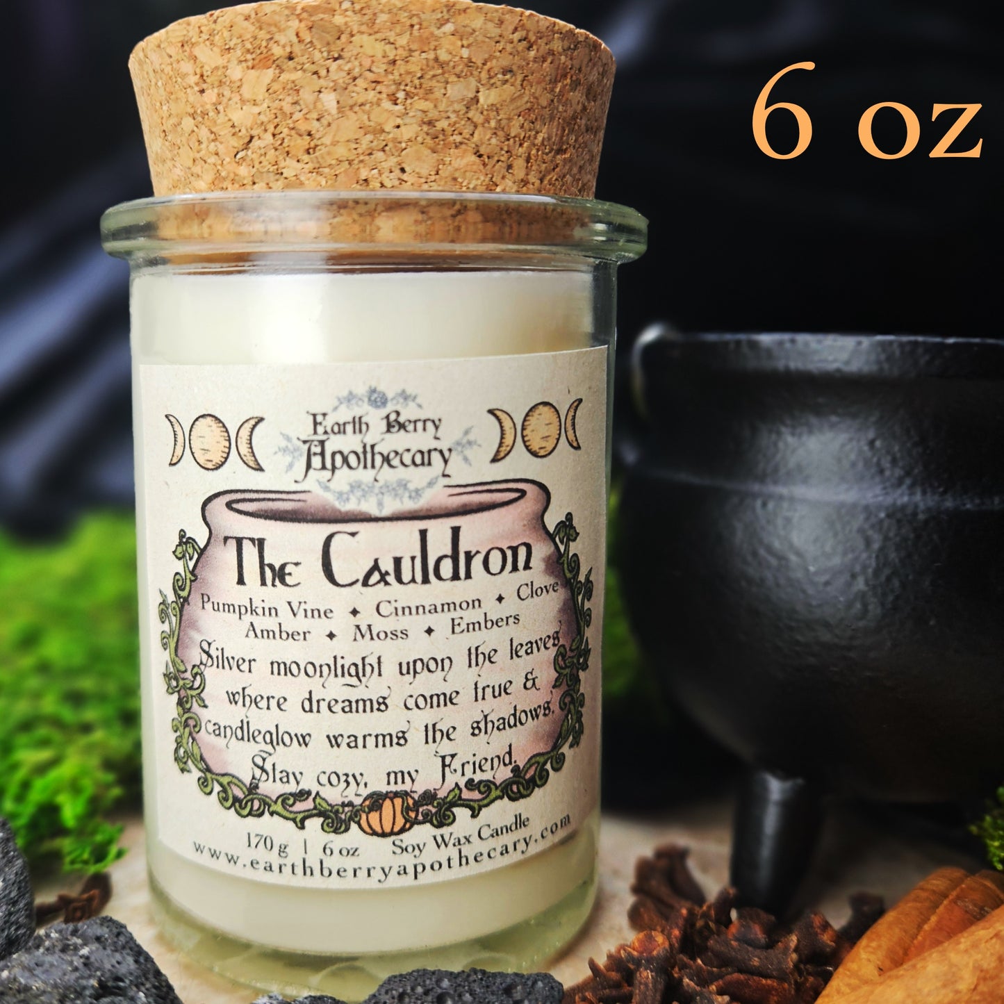 Candle jar labeled 'The Cauldron' from Earth Berry Apothecary with a cork lid, surrounded by nature-themed elements.