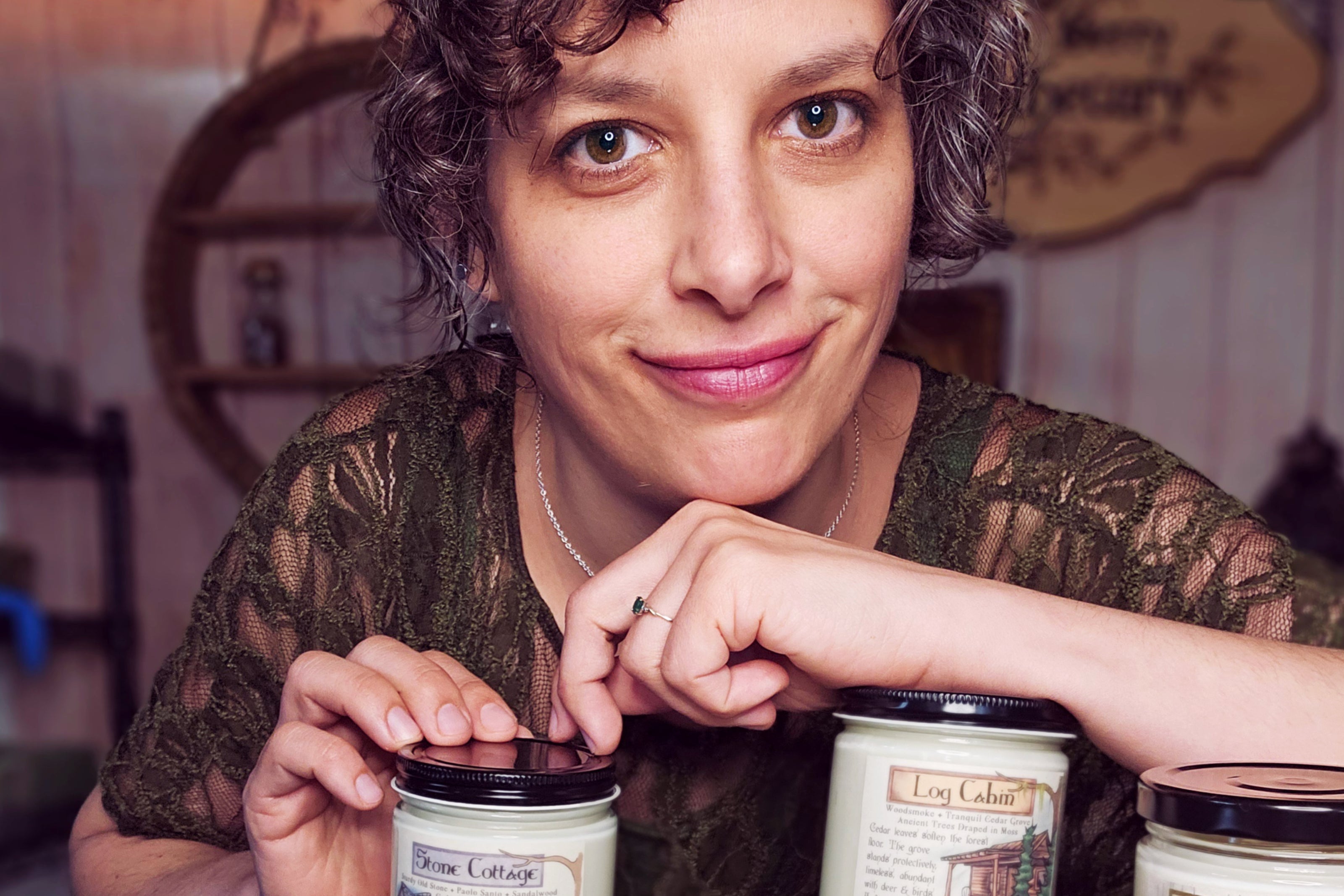 A woman with a friendly smile leaning on a starch of cute fantasy themed candles.