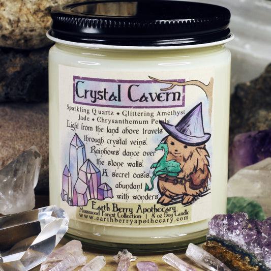 Crystal cavern soy candle with quartz amethyst cactus flower and Jade scents. The hedge witch wears a side pack and holds a green dragon.