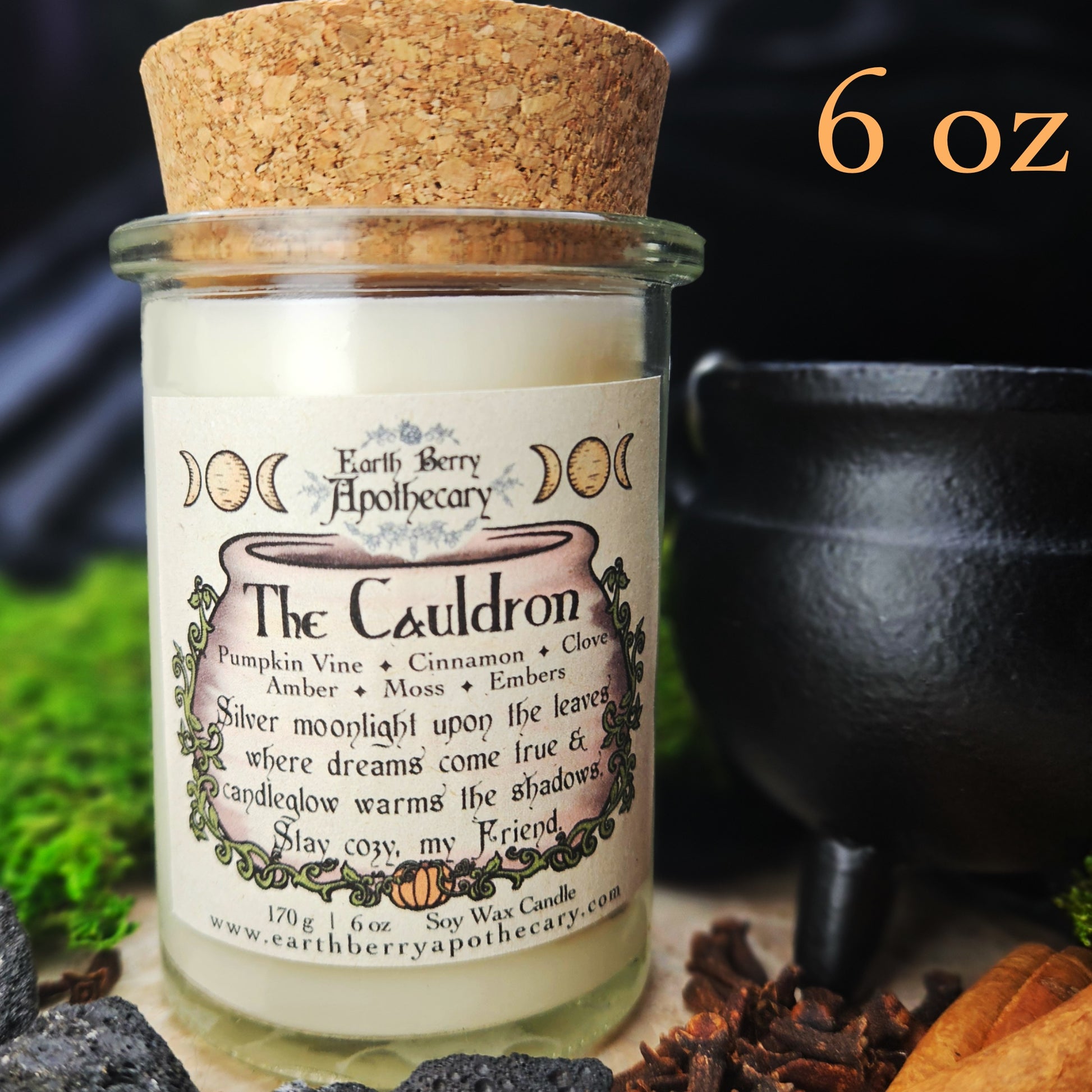 Candle jar labeled 'The Cauldron' from Earth Berry Apothecary with a cork lid, surrounded by nature-themed elements.