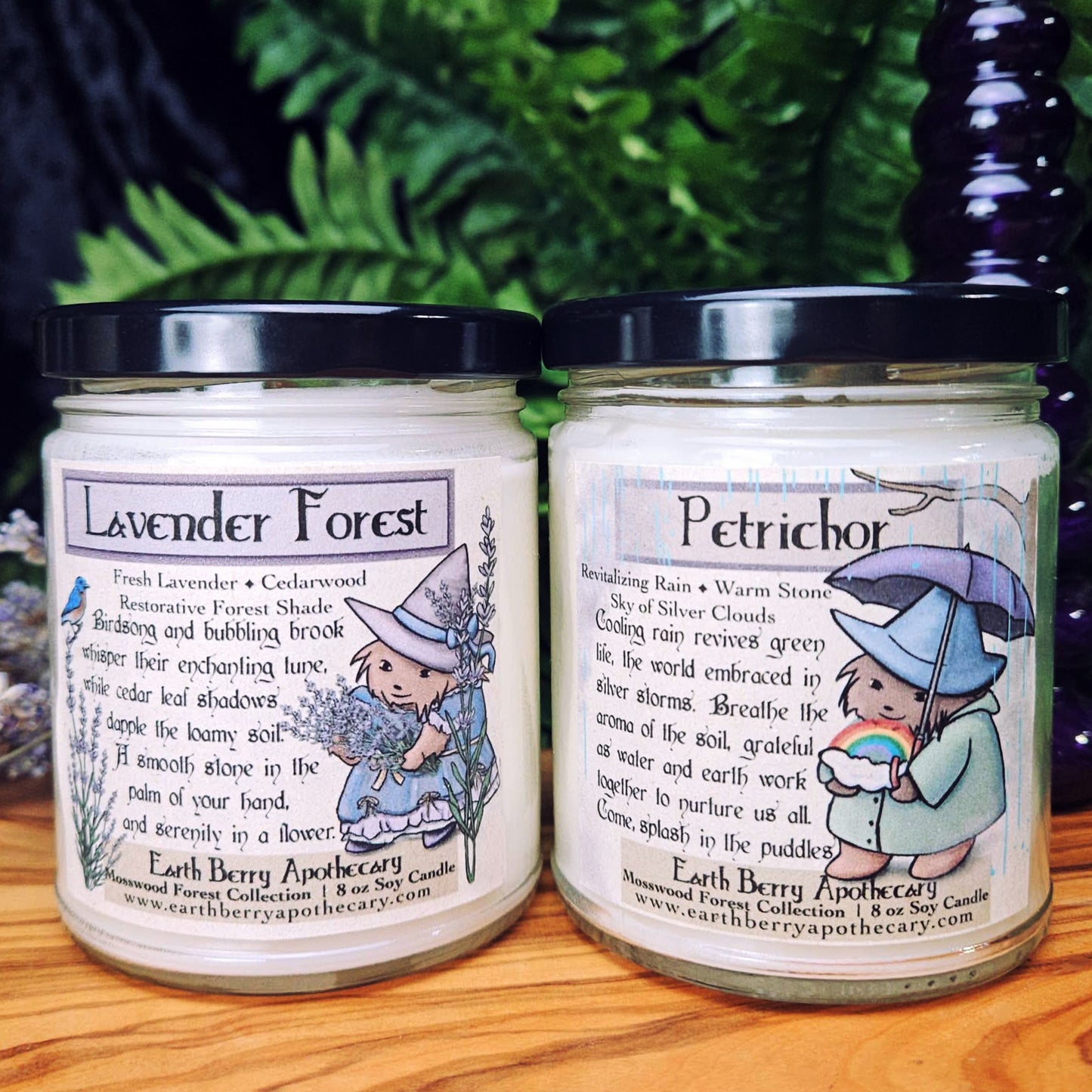 Two jars of Earth Berry Apothecary candles labeled 'Lavender Forest' and 'Petrichor' on a wooden surface with a green leafy background.