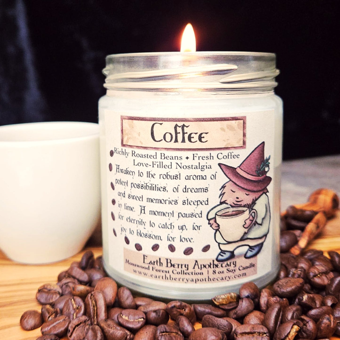 Candle labeled 'Coffee' with a hedgehog in a witch hat character holding a cup, surrounded by coffee beans and a cup on a wooden surface.