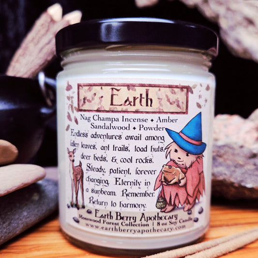 Candle jar labeled 'Earth' with a hedgehog witch and nature-themed design, surrounded by stones.