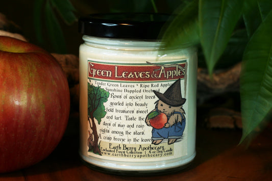 green leaves and apple scented soy candle with hedge witch holding an apple and wearing overalls